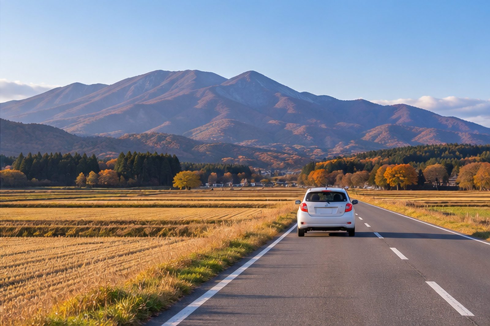 A small car on a country road with mountains in the distance